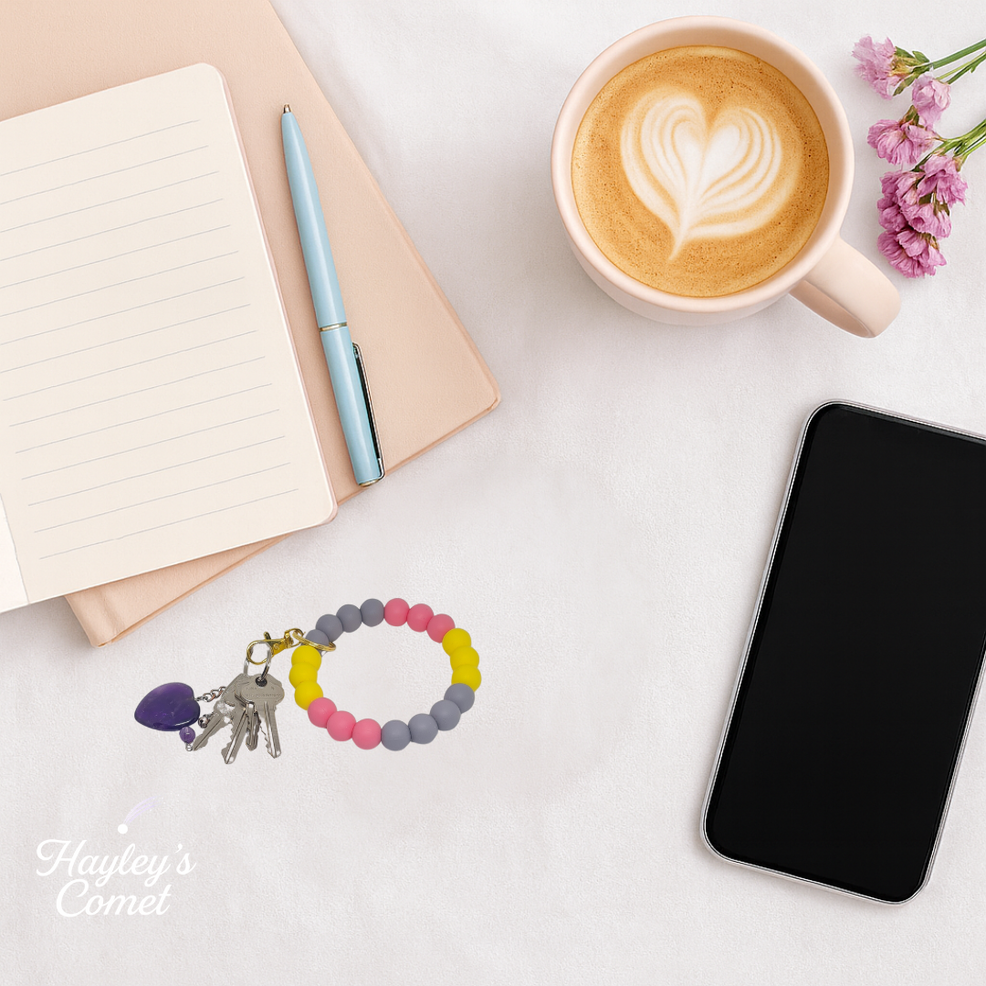 Colorful beaded keychain with keys on a desk beside a cup of coffee, smartphone, and notebook.