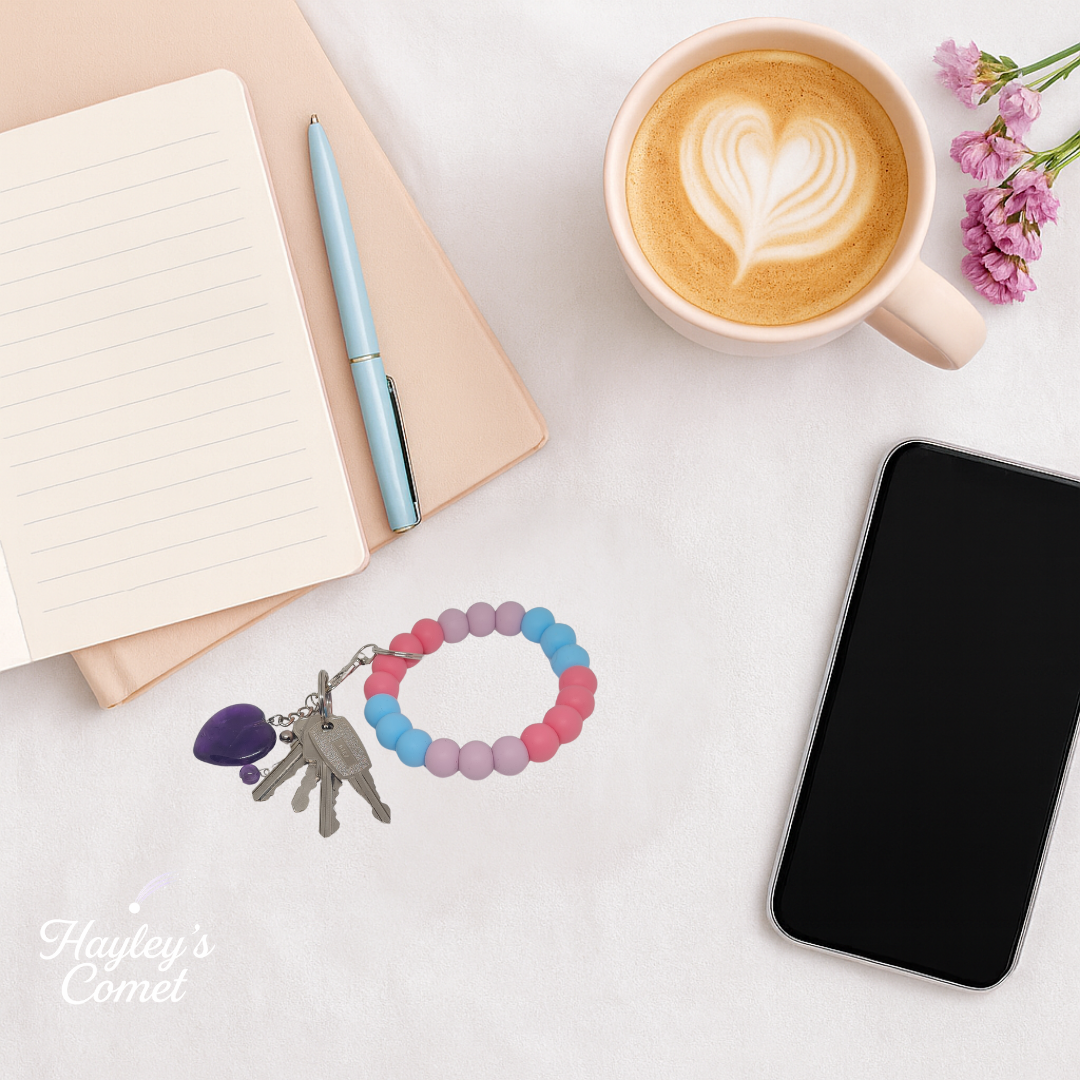Colorful beaded keychain with keys on a desk beside a cup of coffee, smartphone, and notebook.