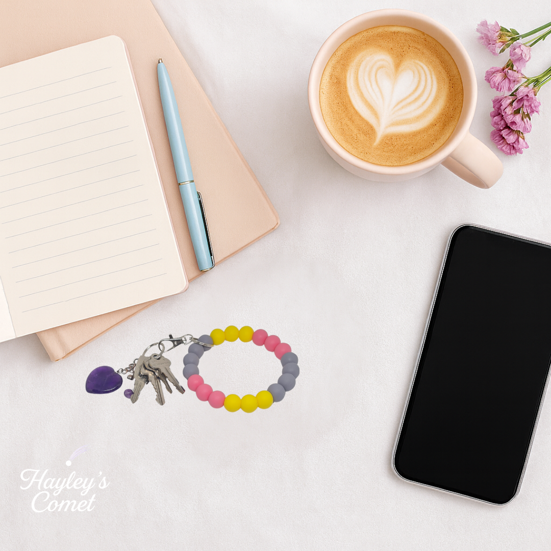 Colorful beaded keychain with keys on a desk beside a cup of coffee, smartphone, and notebook.