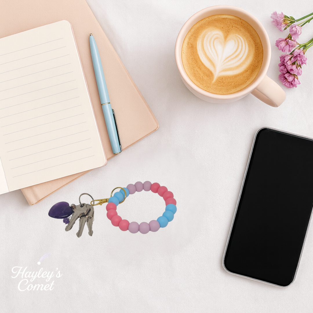 Colorful beaded keychain with keys on a desk beside a cup of coffee, smartphone, and notebook.