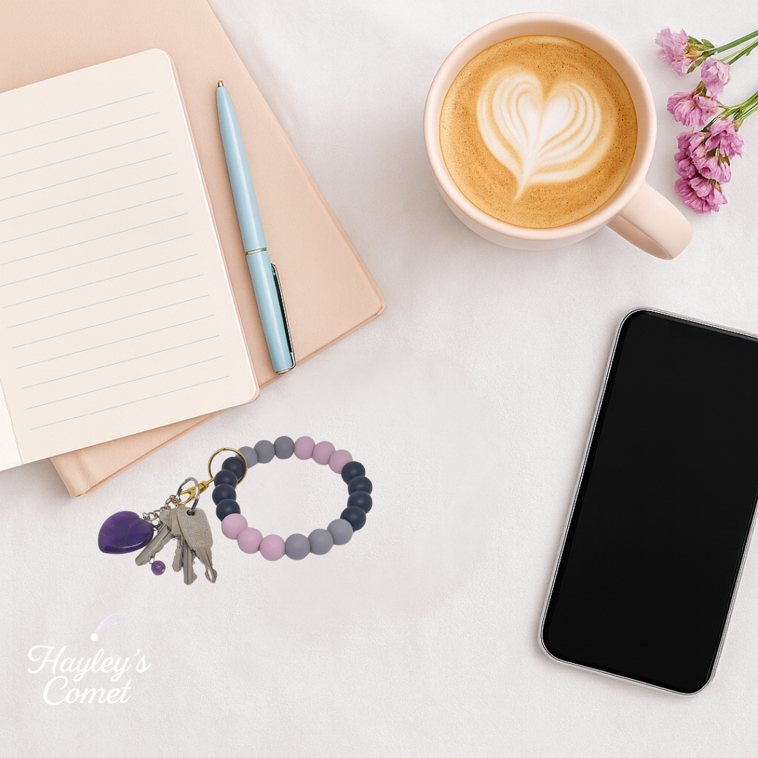 Colorful beaded keychain with keys on a desk beside a cup of coffee, smartphone, and notebook.