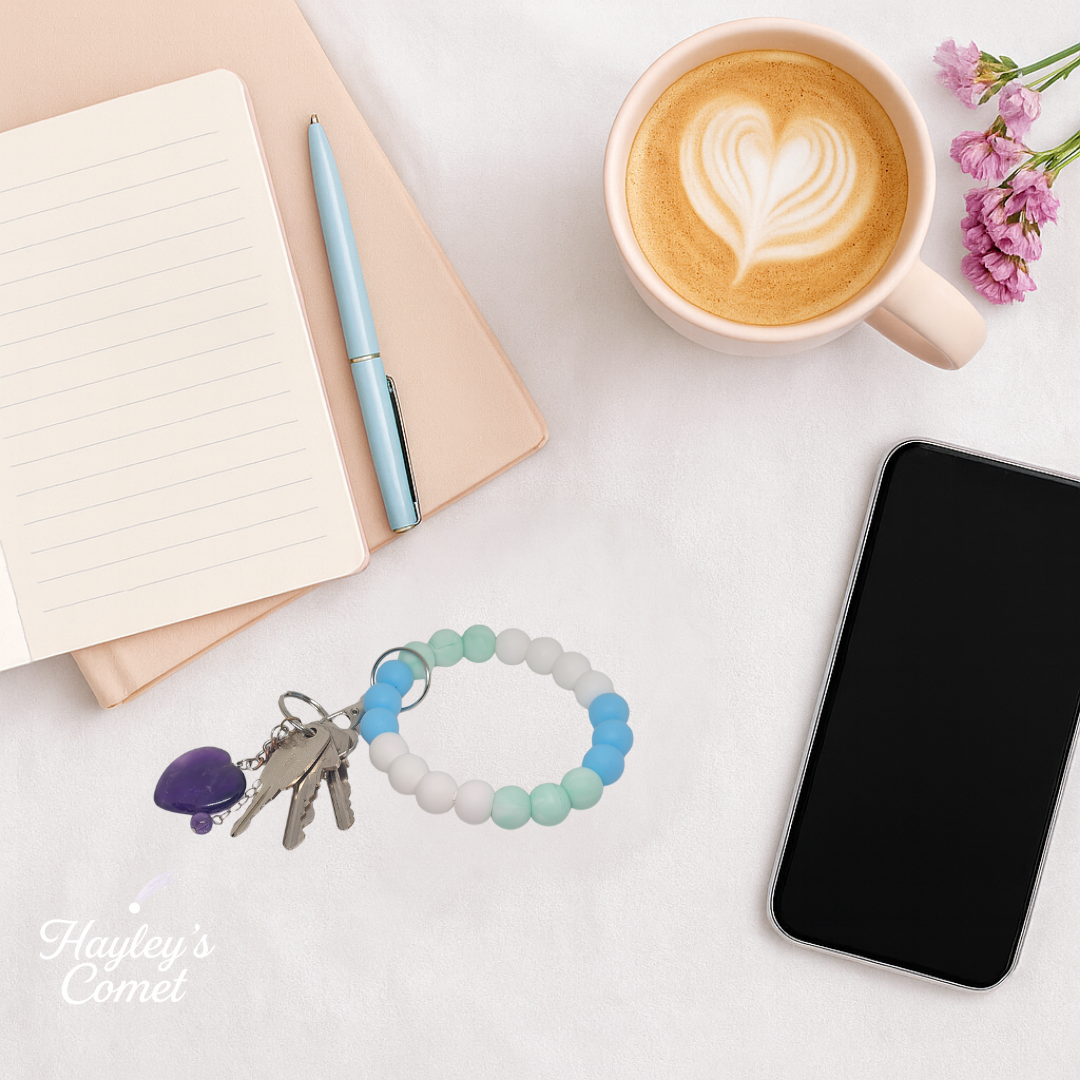 Colorful beaded keychain with keys on a desk beside a cup of coffee, smartphone, and notebook.