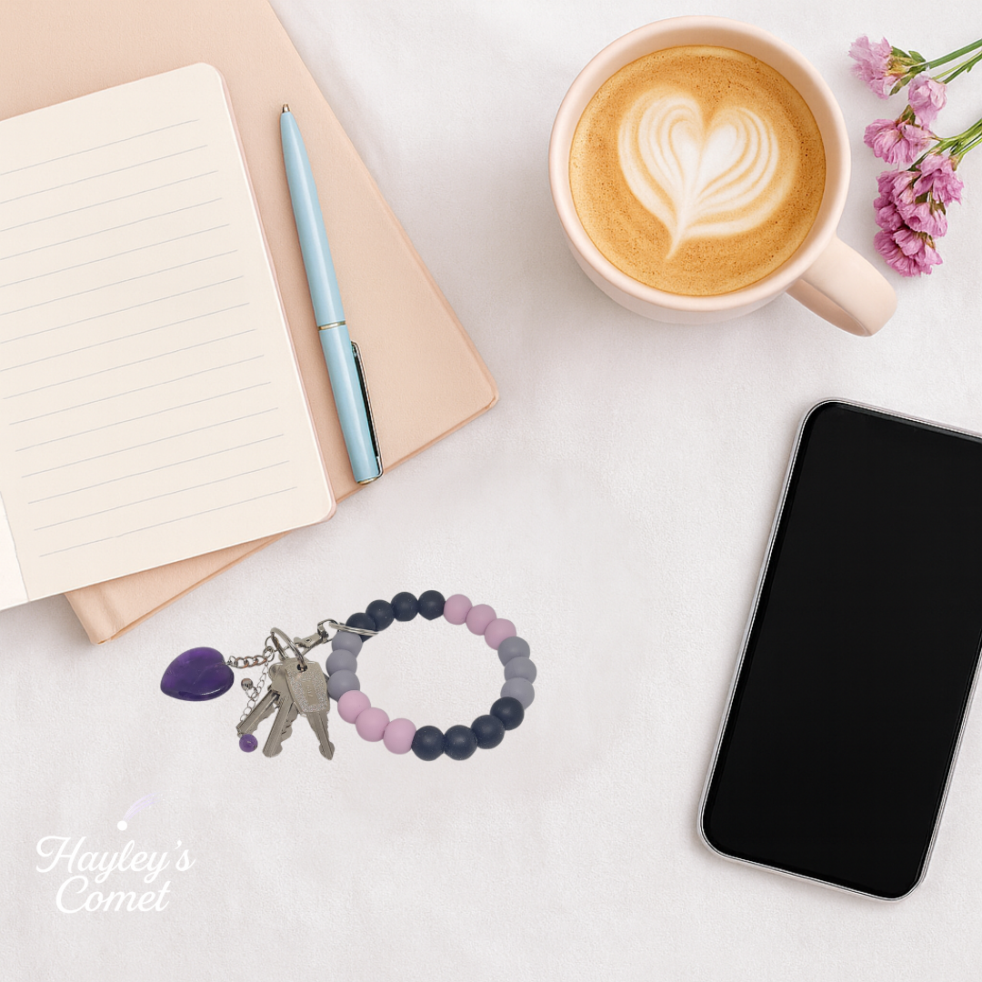 Colorful beaded keychain with keys on a desk beside a cup of coffee, smartphone, and notebook.