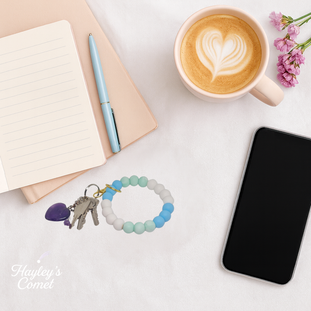 Colorful beaded keychain with keys on a desk beside a cup of coffee, smartphone, and notebook.