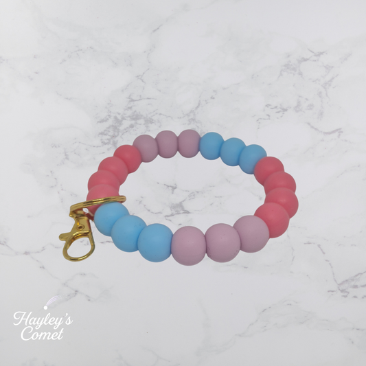 Colorful beaded bracelet with gold clasp on a marble background, branded 'Hayley's Comet'.