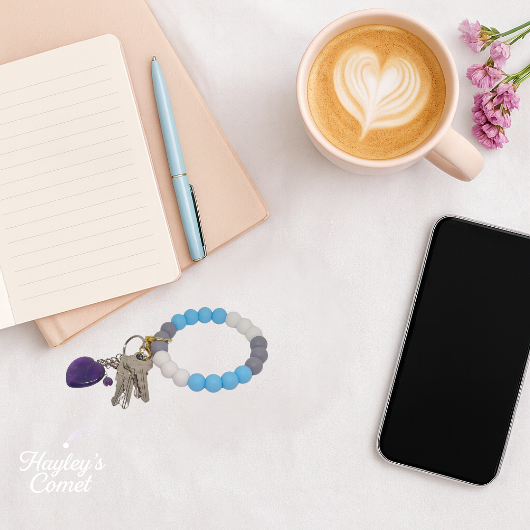 Colorful beaded keychain with keys on a desk beside a cup of coffee, smartphone, and notebook.