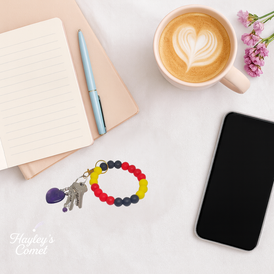 Colorful beaded keychain with keys on a desk beside a cup of coffee, smartphone, and notebook.