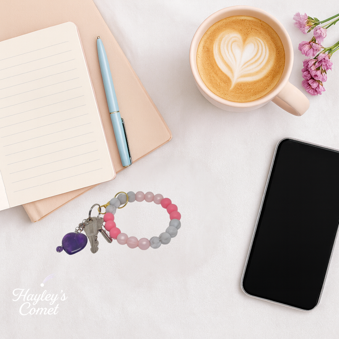 Colorful beaded keychain with keys on a desk beside a cup of coffee, smartphone, and notebook.