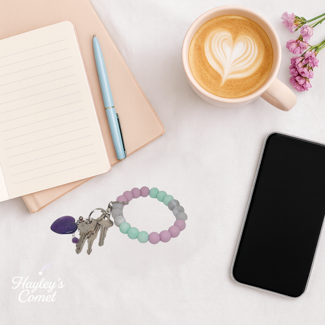 Colorful beaded keychain with keys on a desk beside a cup of coffee, smartphone, and notebook.