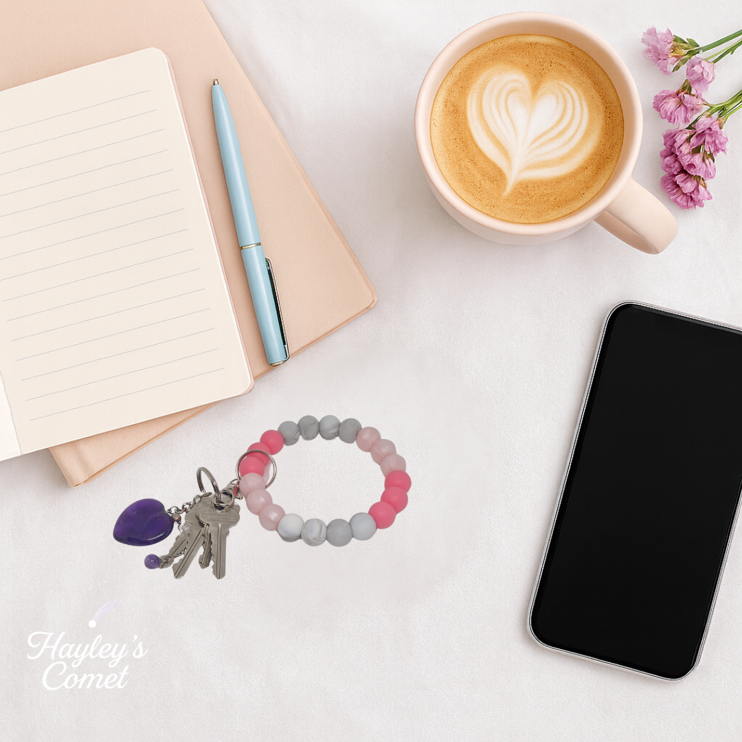 Colorful beaded keychain with keys on a desk beside a cup of coffee, smartphone, and notebook.